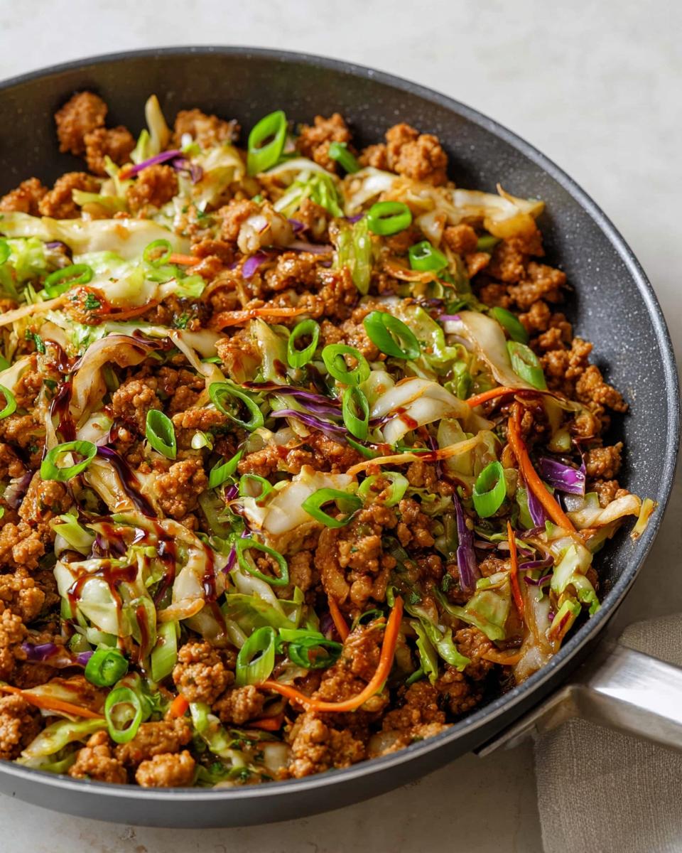 A close-up of a 20-minute pork skillet with ground pork, cabbage, carrots, and green onions, drizzled with sauce. Perfect for dinner ideas in 20 minutes.