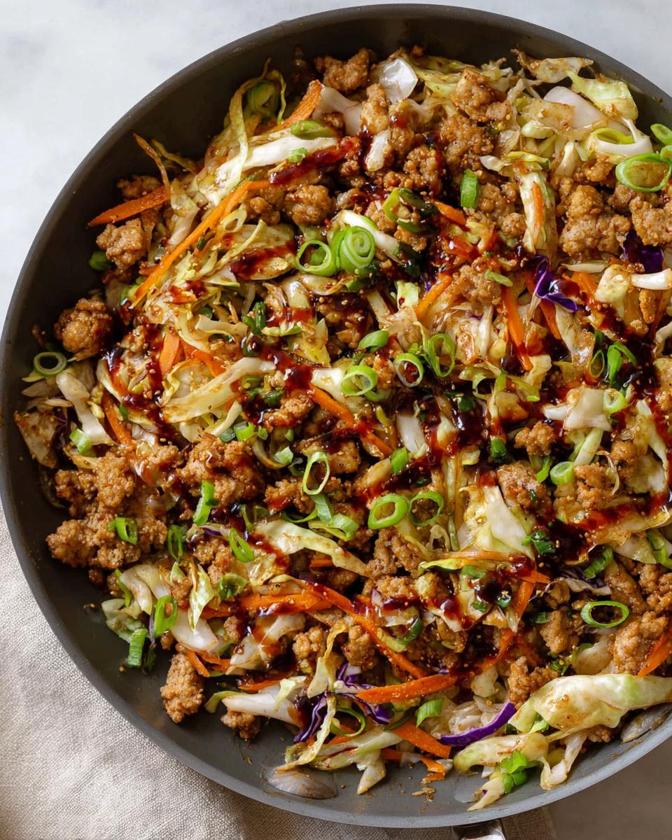 A close-up overhead view of a 20-minute pork skillet dish with ground pork, cabbage, carrots, and green onions, drizzled with sauce.