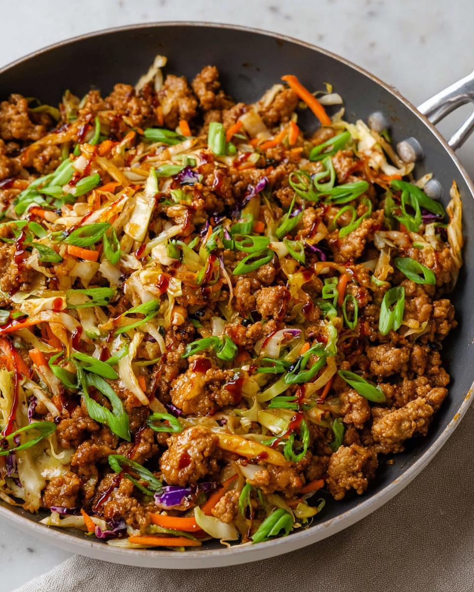 A close-up of a 20-minute pork skillet with ground pork, cabbage, carrots, and green onions, drizzled with sauce. Perfect for quick dinner ideas.
