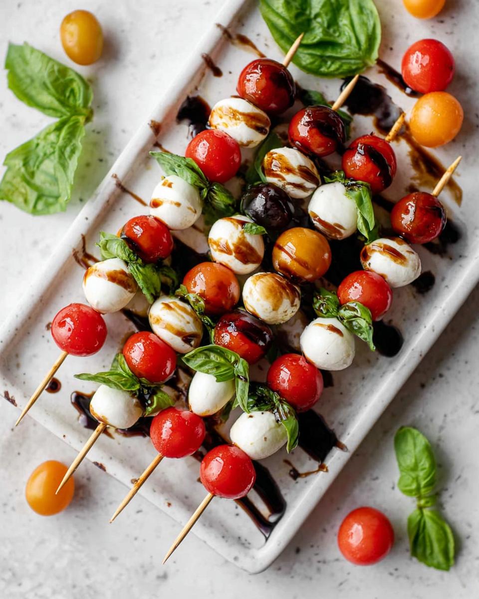 Close-up overhead view of several 5-Ingredient Caprese Skewers featuring mozzarella balls, cherry tomatoes, and basil drizzled with balsamic glaze.