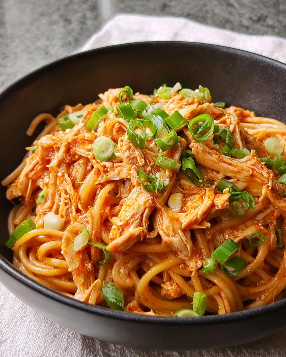 A bowl of noodles topped with shredded chicken in a creamy sauce and garnished with chopped green onions. A great 5-Ingredient Dinner Idea.