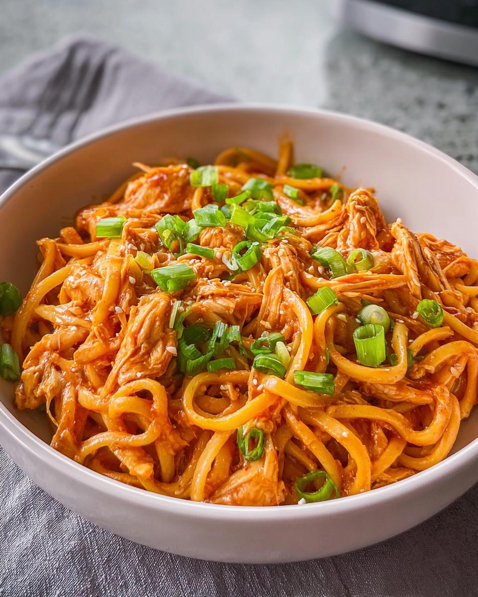 A bowl of shredded chicken noodles with a creamy orange sauce, topped with chopped green onions and sesame seeds. Part of 5-Ingredient Dinner Ideas.
