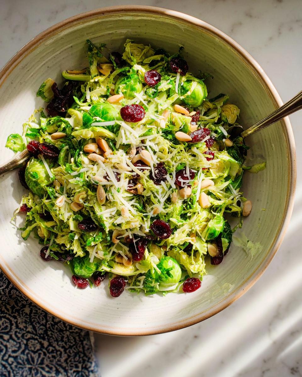 A bowl of shredded Brussels sprouts salad with dried cranberries, slivered almonds, and shredded Parmesan cheese, perfect for 5-Ingredient Thanksgiving Salad Recipes.