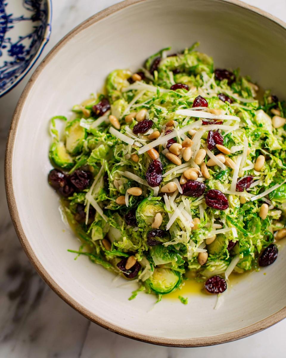 A vibrant 5-ingredient Thanksgiving salad featuring shredded Brussels sprouts, dried cranberries, pine nuts, and shaved cheese.