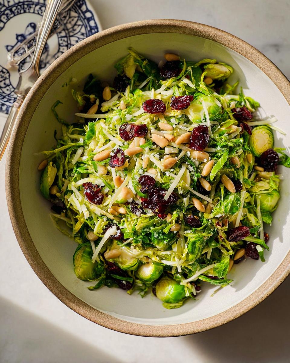 A close-up of a vibrant 5-Ingredient Thanksgiving Salad featuring shredded Brussels sprouts, dried cranberries, pine nuts, and cheese.