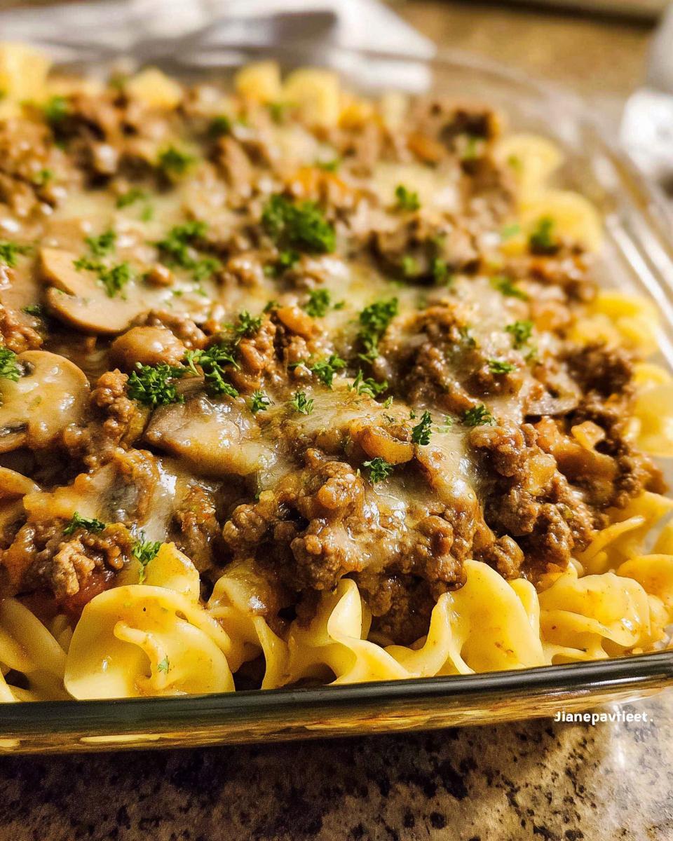 Close-up of a baked casserole featuring ground beef, mushrooms, melted cheese, and egg noodles, resembling a Beef Enchilada Casserole.