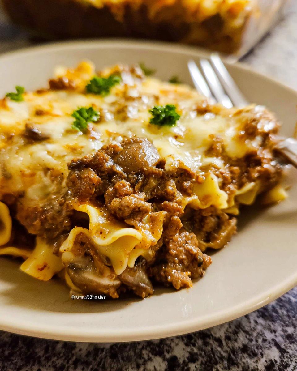 Close-up of a serving of rich Beef Enchilada Casserole topped with melted cheese and parsley.