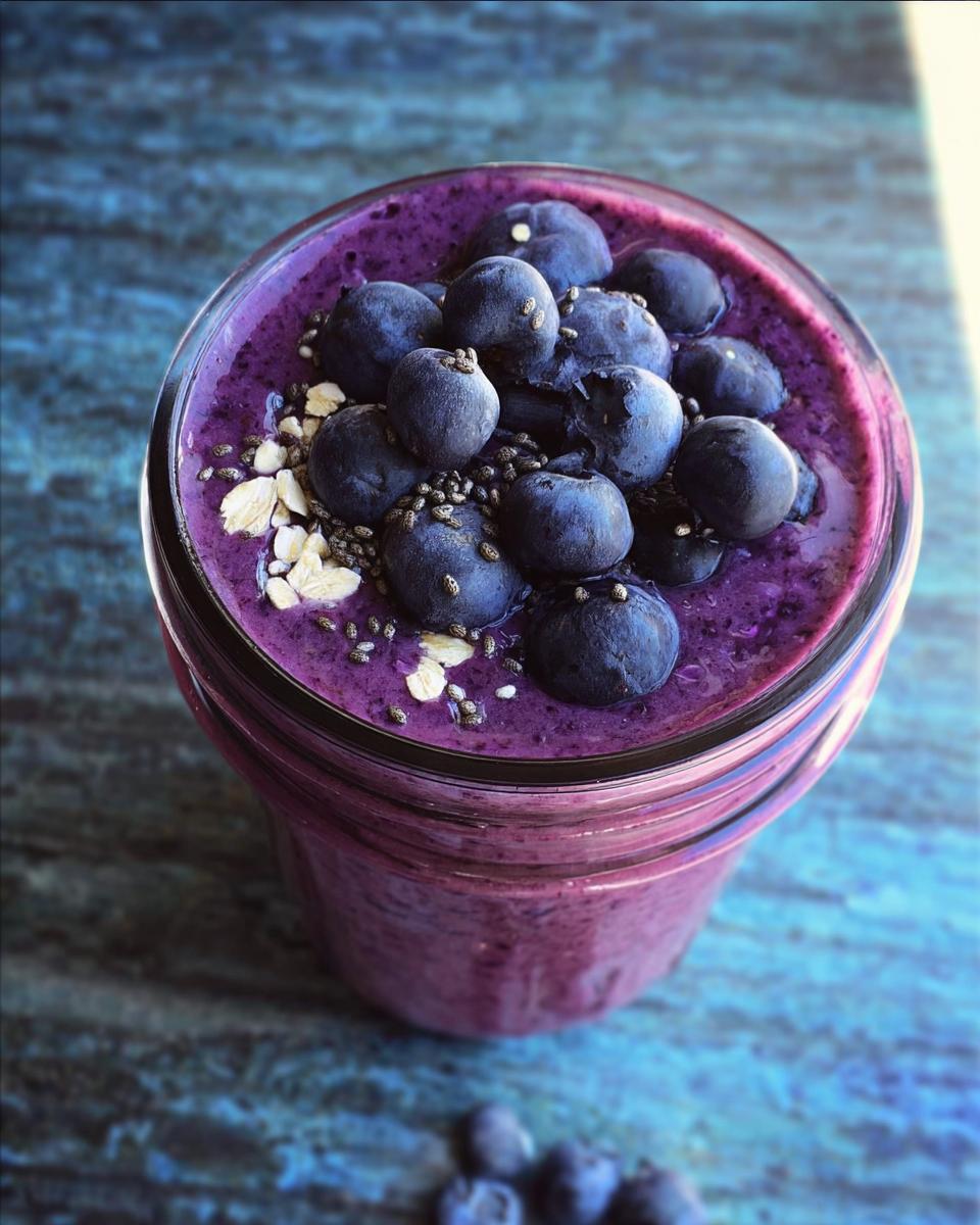 Overhead view of a thick, purple Blueberry Oat Breakfast Smoothie topped with fresh blueberries, oats, and chia seeds.