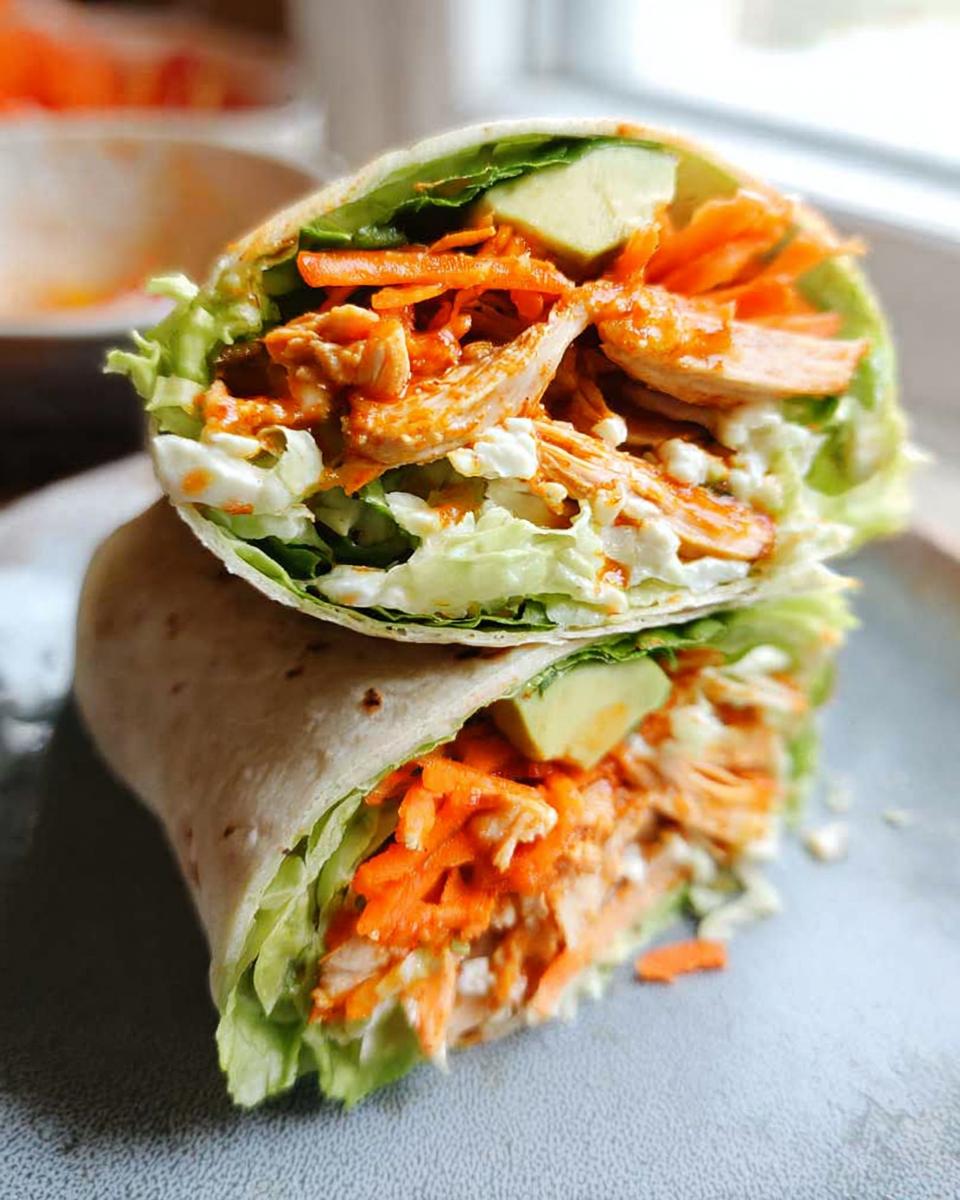 Close-up of Buffalo Chicken Lettuce Wraps cut in half, revealing shredded chicken, avocado, shredded carrots, and lettuce.