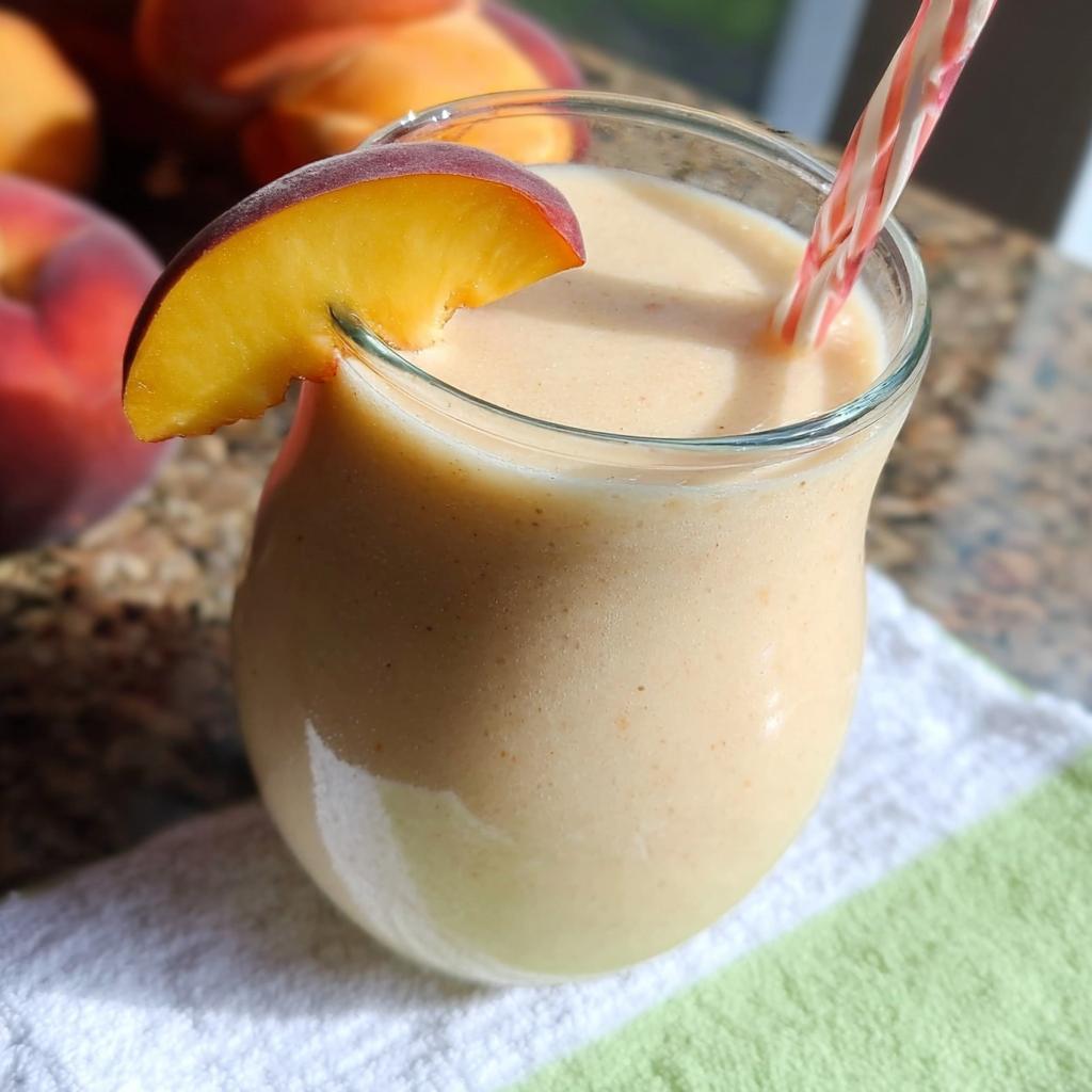 A close-up of a creamy Peach Yogurt Smoothie garnished with a fresh peach slice and a striped straw.
