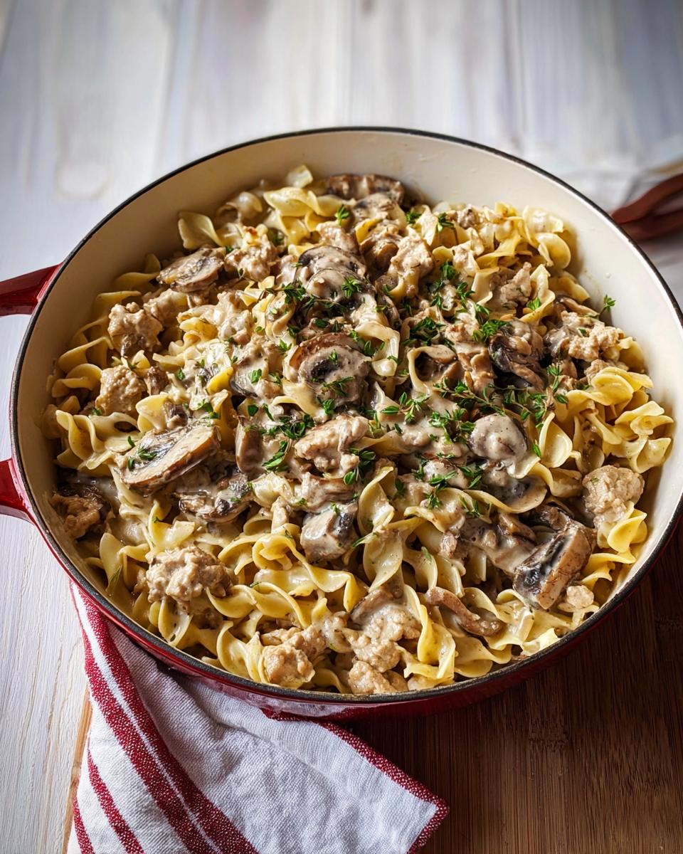 A close-up of Creamy Turkey Stroganoff with egg noodles and mushrooms, garnished with fresh herbs in a red skillet.