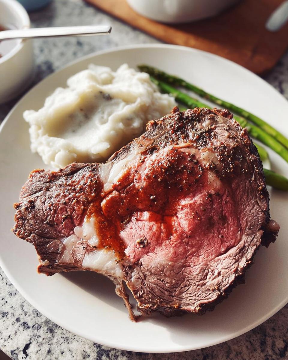 A thick slice of perfectly cooked Easy Prime Rib, medium-rare, served with mashed potatoes and asparagus.