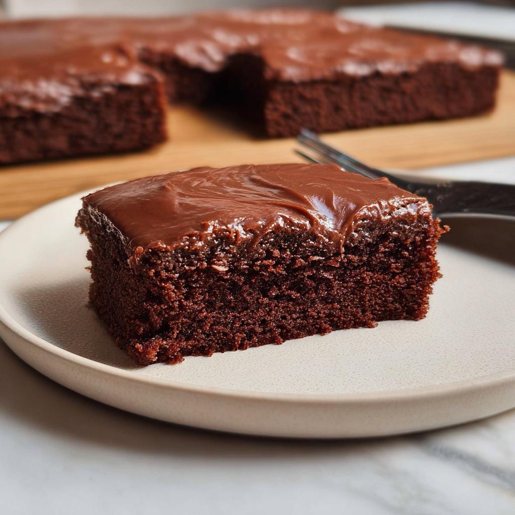 A square slice of rich, dark Easy Snacking Sheet Cake topped with glossy chocolate frosting on a plate.