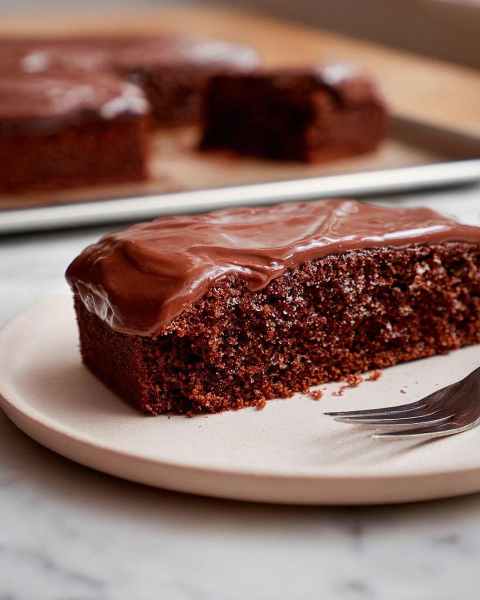 A close-up of a moist slice of Easy Snacking Sheet Cake topped with smooth chocolate frosting on a plate.
