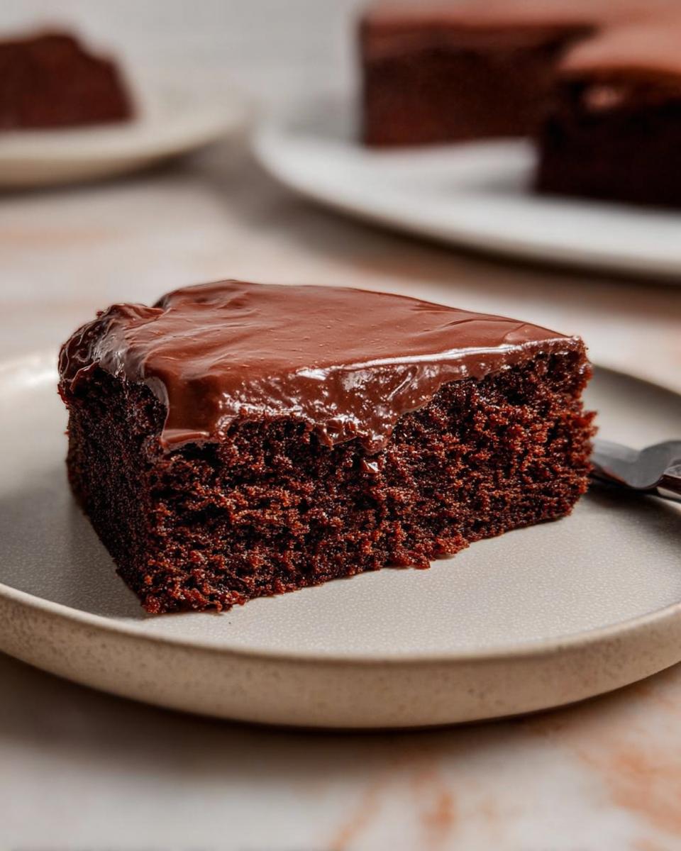 A close-up of a moist slice of Easy Snacking Sheet Cake topped with glossy chocolate frosting on a plate.