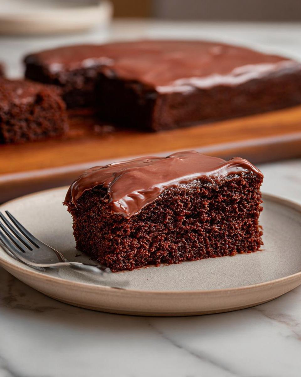 A moist slice of Easy Snacking Sheet Cake topped with glossy chocolate frosting on a plate.