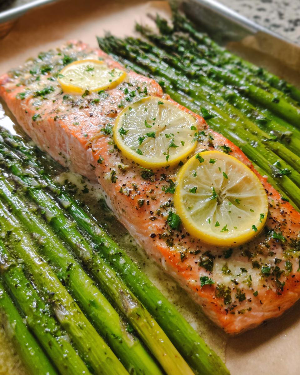 Close-up of baked Garlic Butter Salmon & Asparagus topped with lemon slices and herbs.