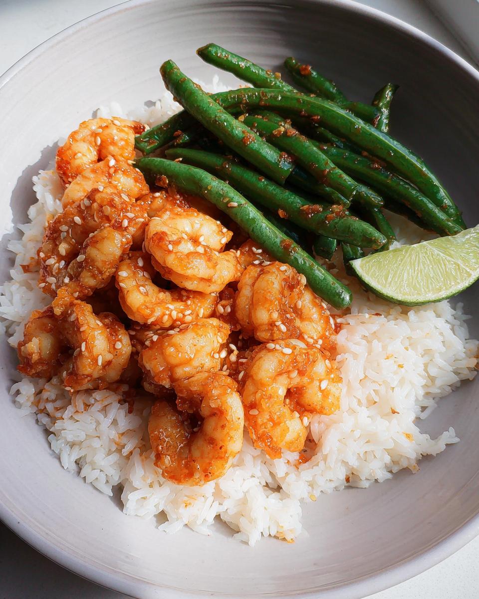 A bowl of Garlic Chili Shrimp With Jasmine Rice, topped with sesame seeds and served with green beans and a lime wedge.