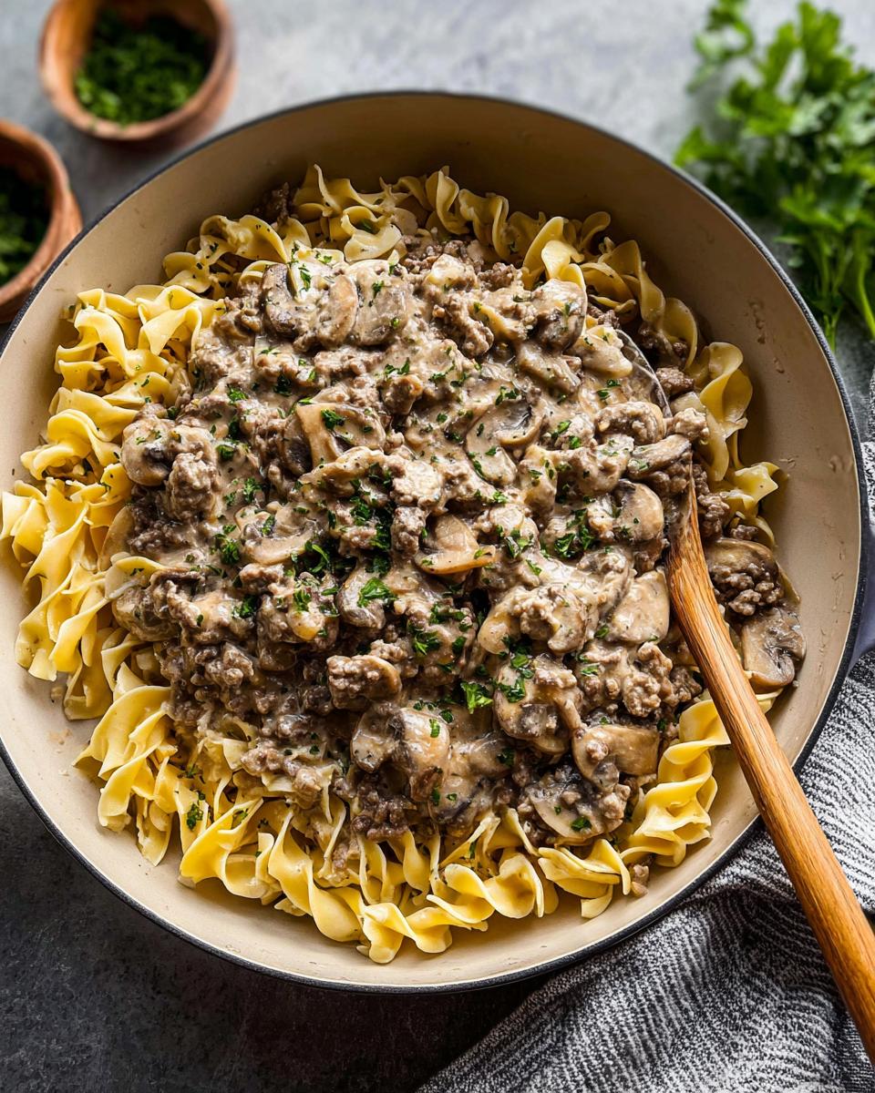 A skillet filled with Ground Beef Stroganoff served over wide egg noodles, topped with fresh parsley.