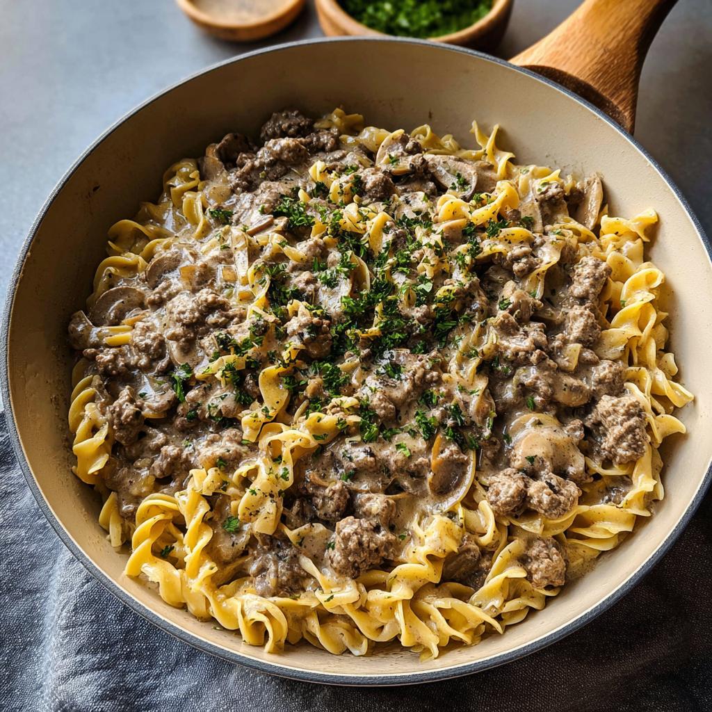A creamy skillet full of Ground Beef Stroganoff served over wide egg noodles and topped with fresh parsley.
