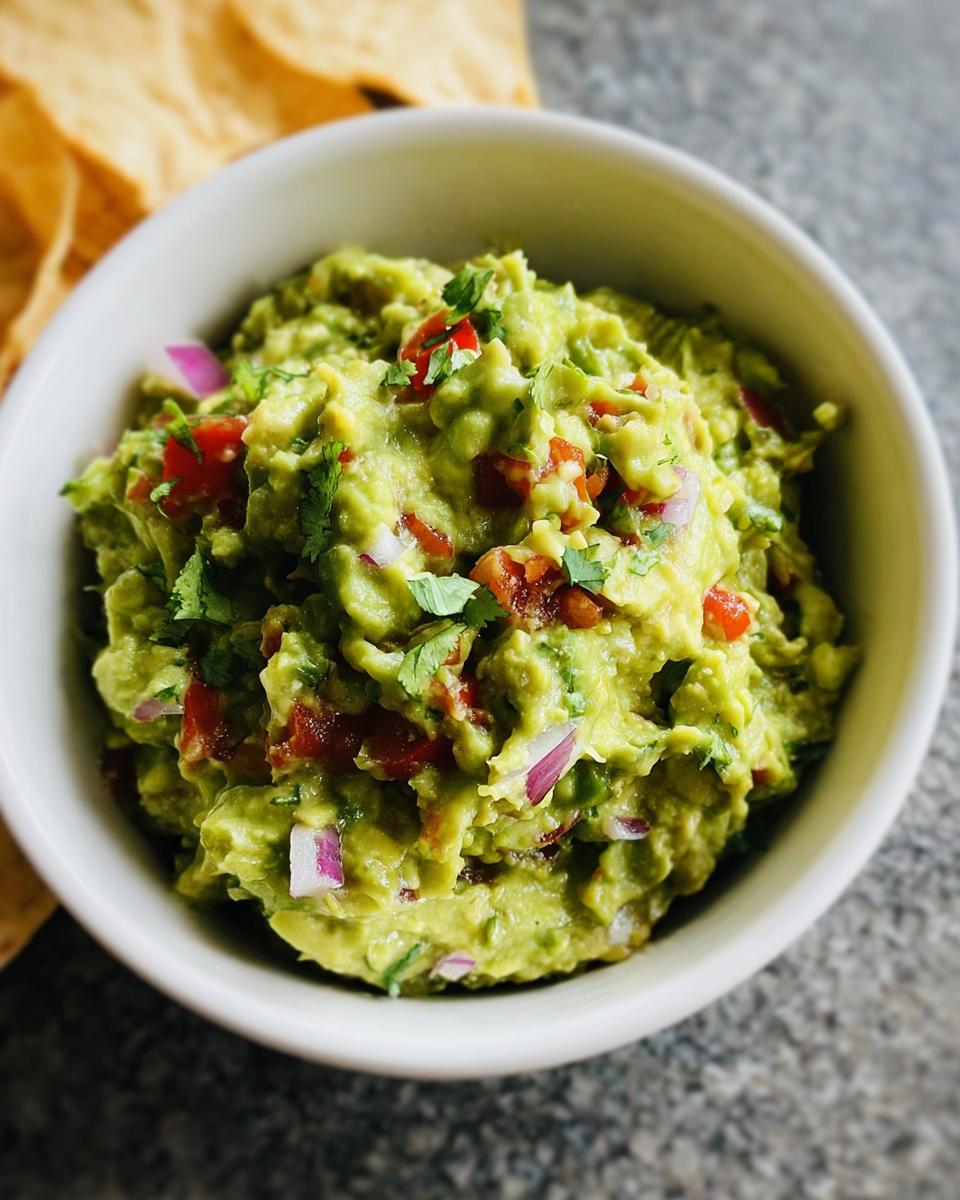 Close-up of chunky Guacamole with Lime and Cilantro, topped with red onion and tomato, served with tortilla chips.