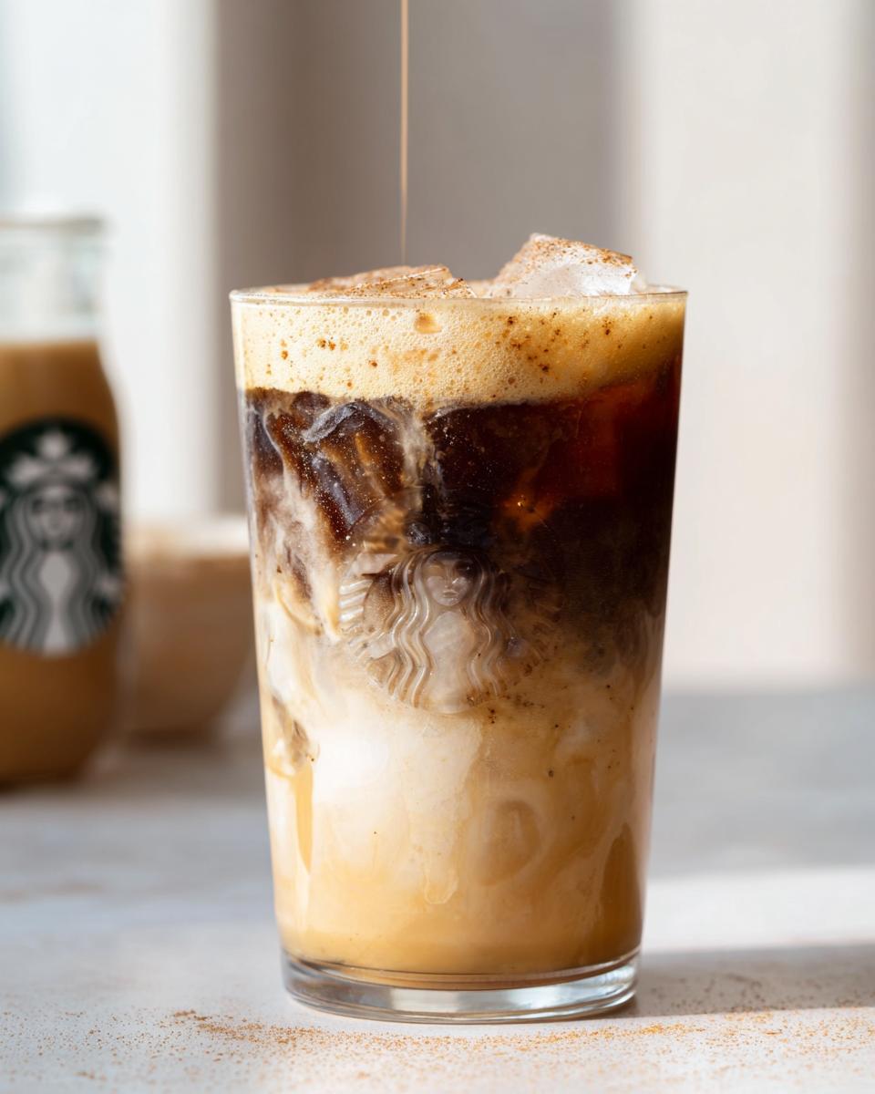A tall glass of Iced Brown Sugar Oatmilk Shaken Espresso with layers of oat milk, espresso, ice, and foam, being topped with a drizzle.