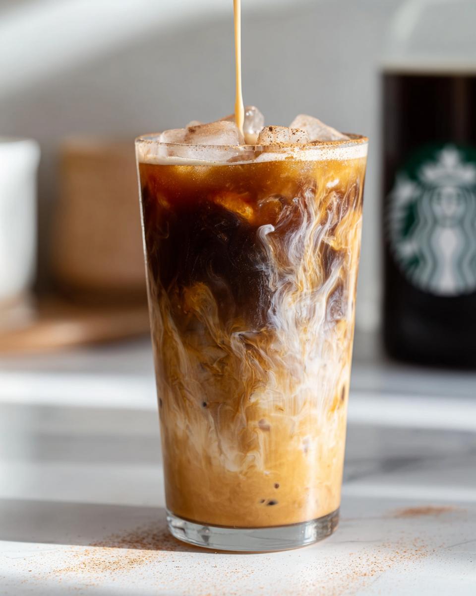 A tall glass of Iced Brown Sugar Oatmilk Shaken Espresso with oat milk being poured over ice and espresso, creating swirls.