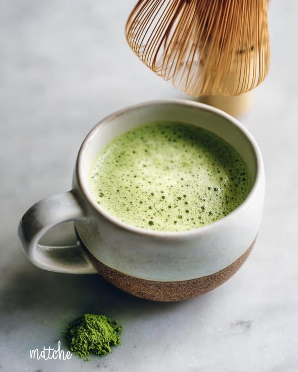 A freshly prepared Matcha Green Tea Latte in a rustic mug, with matcha powder and a bamboo whisk nearby.