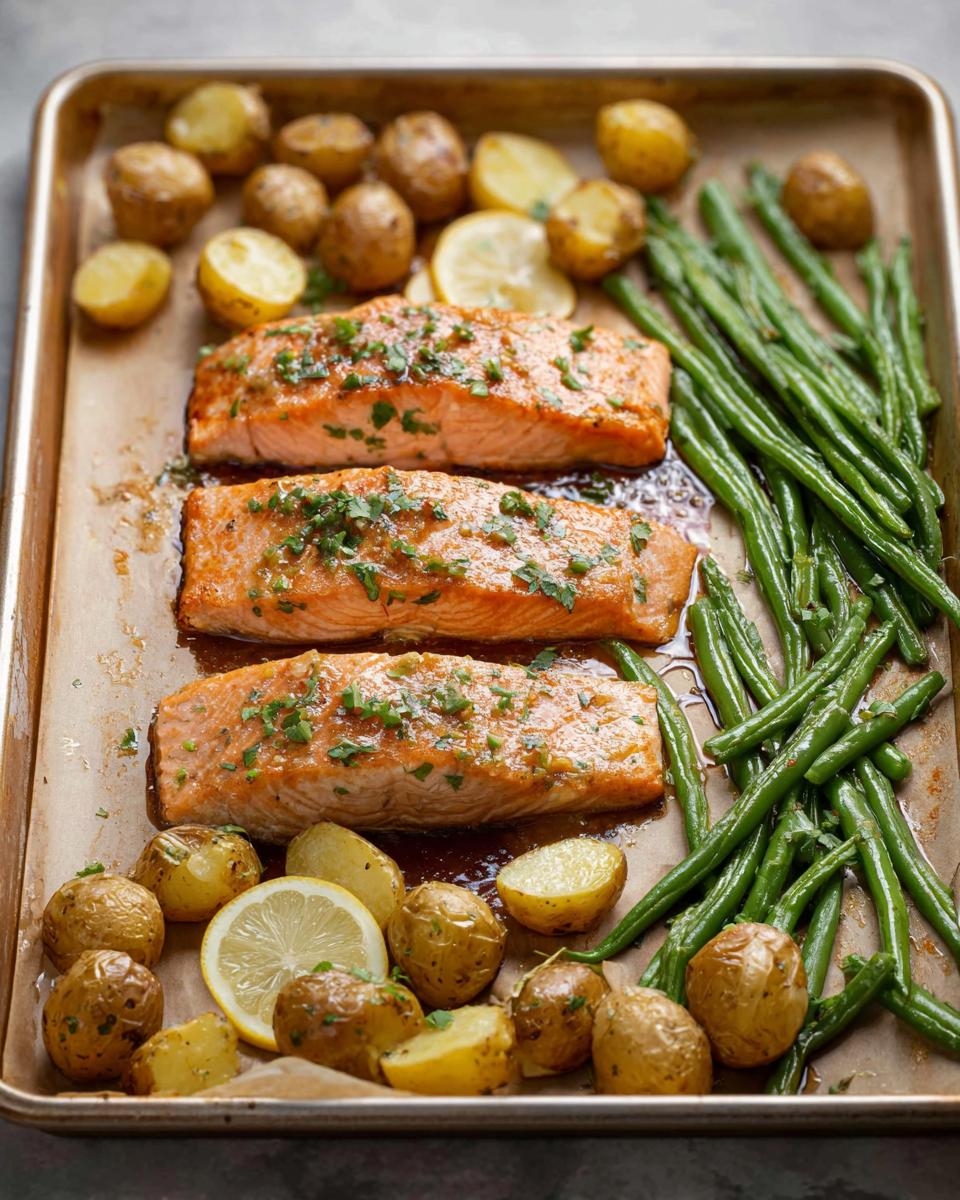 Three cooked salmon fillets with roasted potatoes and green beans on a sheet pan, a Sheet-Pan Salmon & Veggies recipe.
