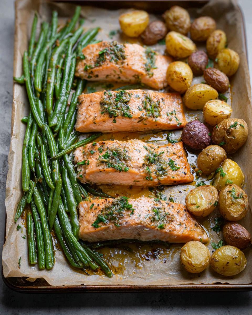 Four fillets of seasoned salmon with green beans and roasted potatoes on a sheet pan.