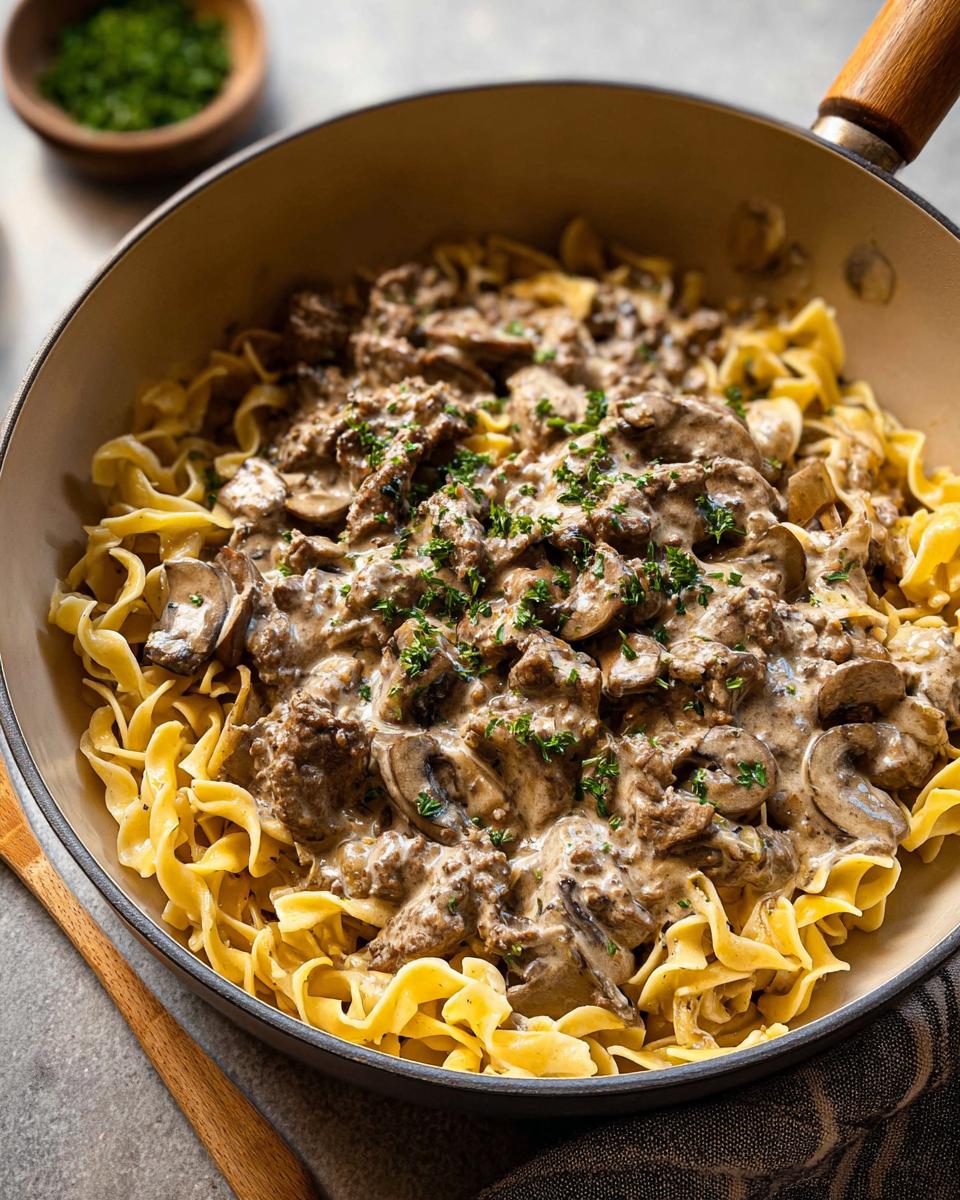 A skillet filled with creamy Ground Beef Stroganoff served over wide egg noodles and garnished with parsley.