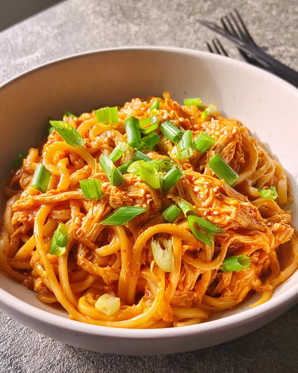 Close-up of a bowl of spicy chicken noodles topped with chopped green onions and sesame seeds, part of 5-Ingredient Dinner Ideas.