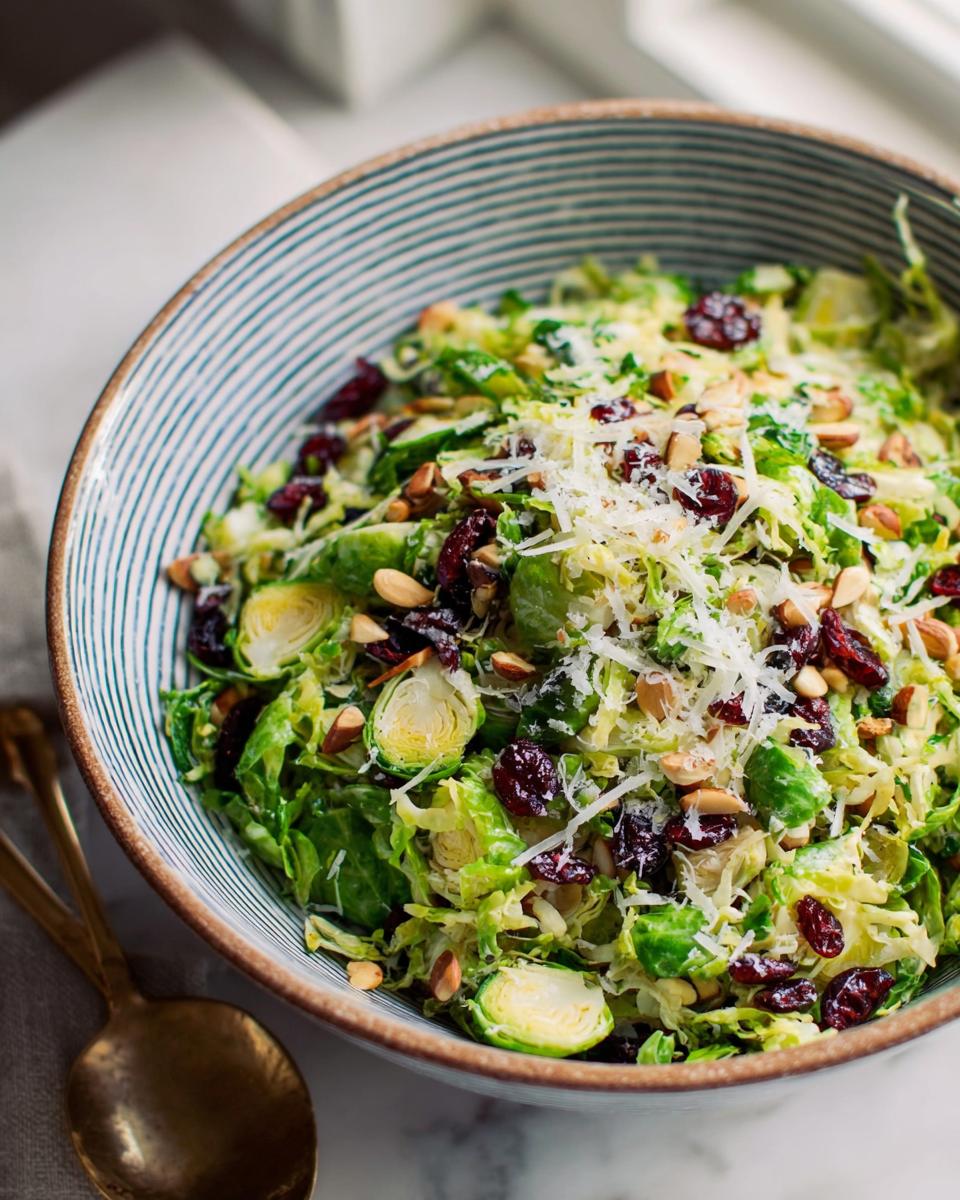A vibrant bowl of Thanksgiving salad featuring shredded Brussels sprouts, dried cranberries, slivered almonds, and grated Parmesan cheese.