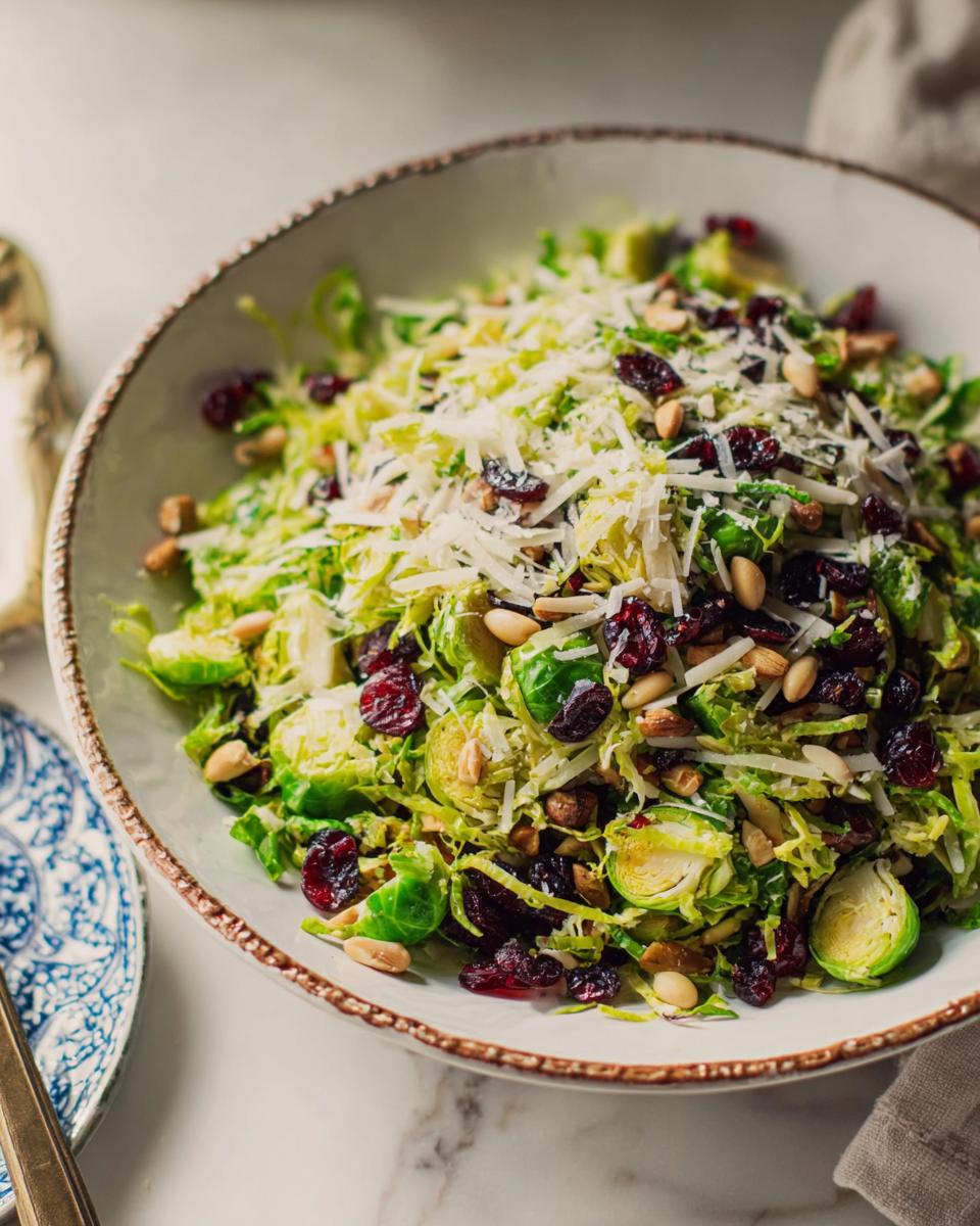 A vibrant bowl of Thanksgiving salad featuring shredded Brussels sprouts, dried cranberries, pine nuts, and grated Parmesan cheese.