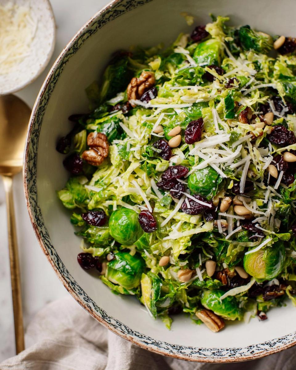 A vibrant Thanksgiving salad featuring shredded Brussels sprouts, whole Brussels sprouts, dried cranberries, walnuts, pine nuts, and shredded Parmesan cheese.