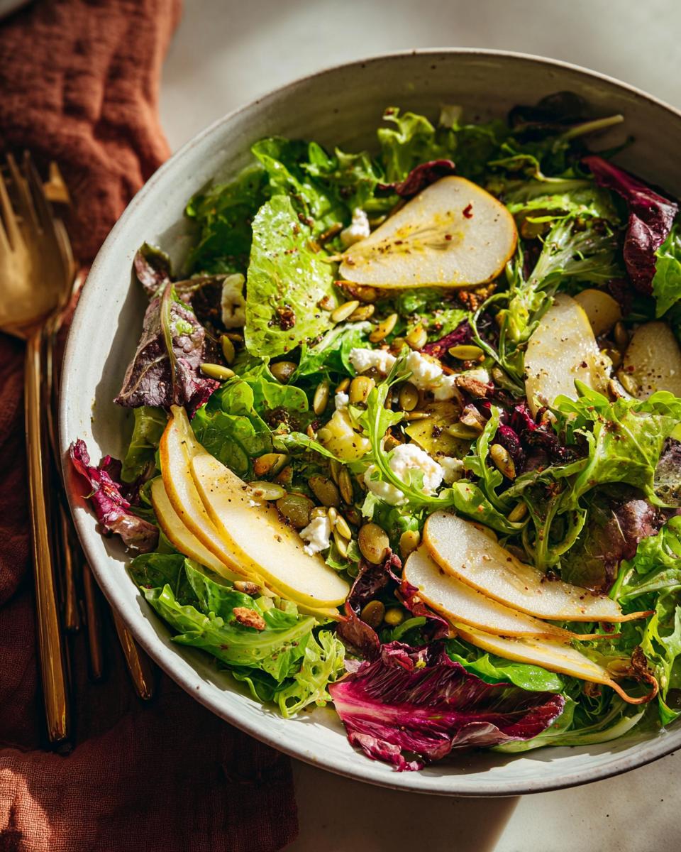 A vibrant Thanksgiving salad recipe featuring fresh greens, sliced pears, crumbled cheese, and pumpkin seeds.