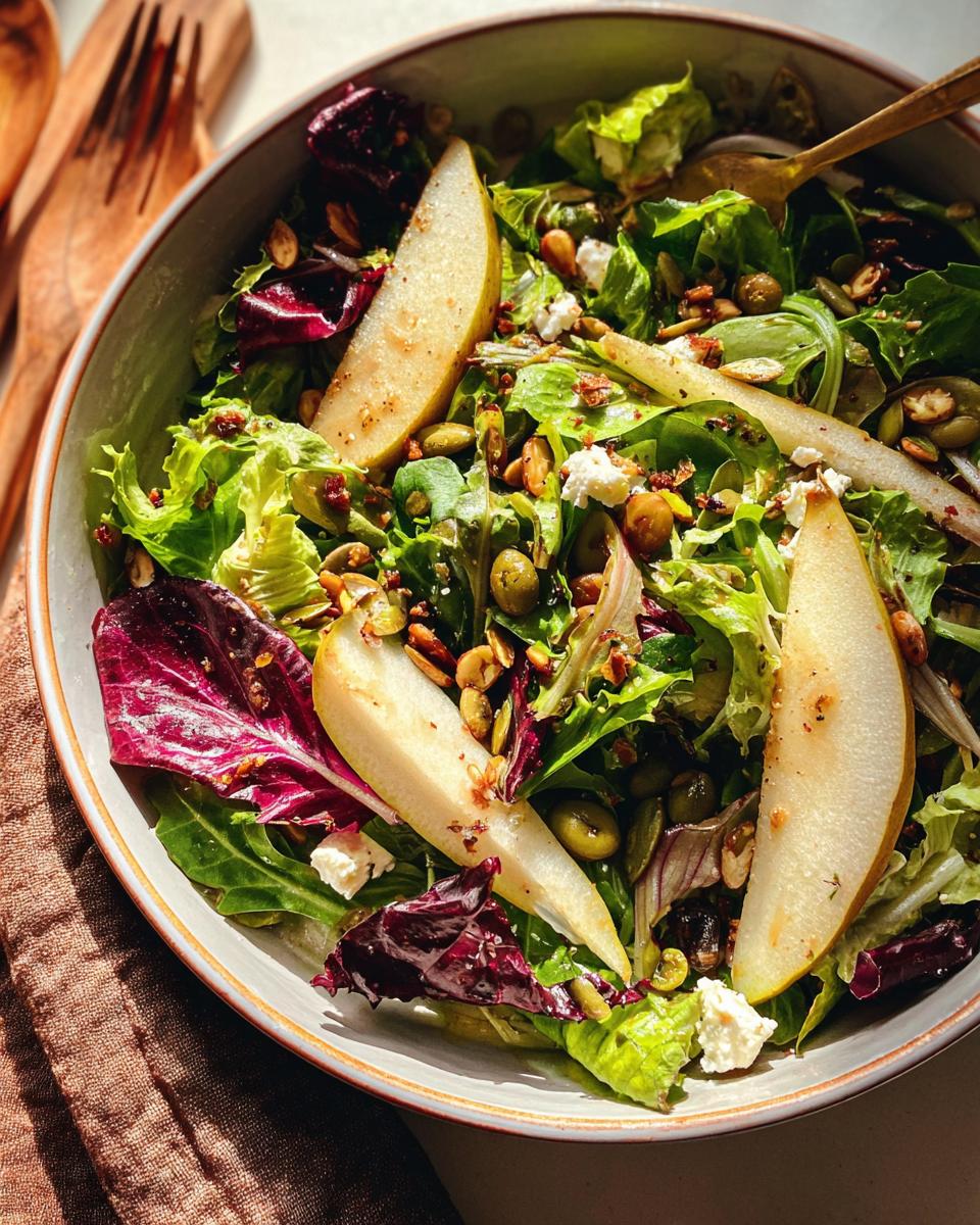A vibrant Thanksgiving salad recipe featuring fresh greens, sliced pears, crumbled feta, olives, and mixed nuts.