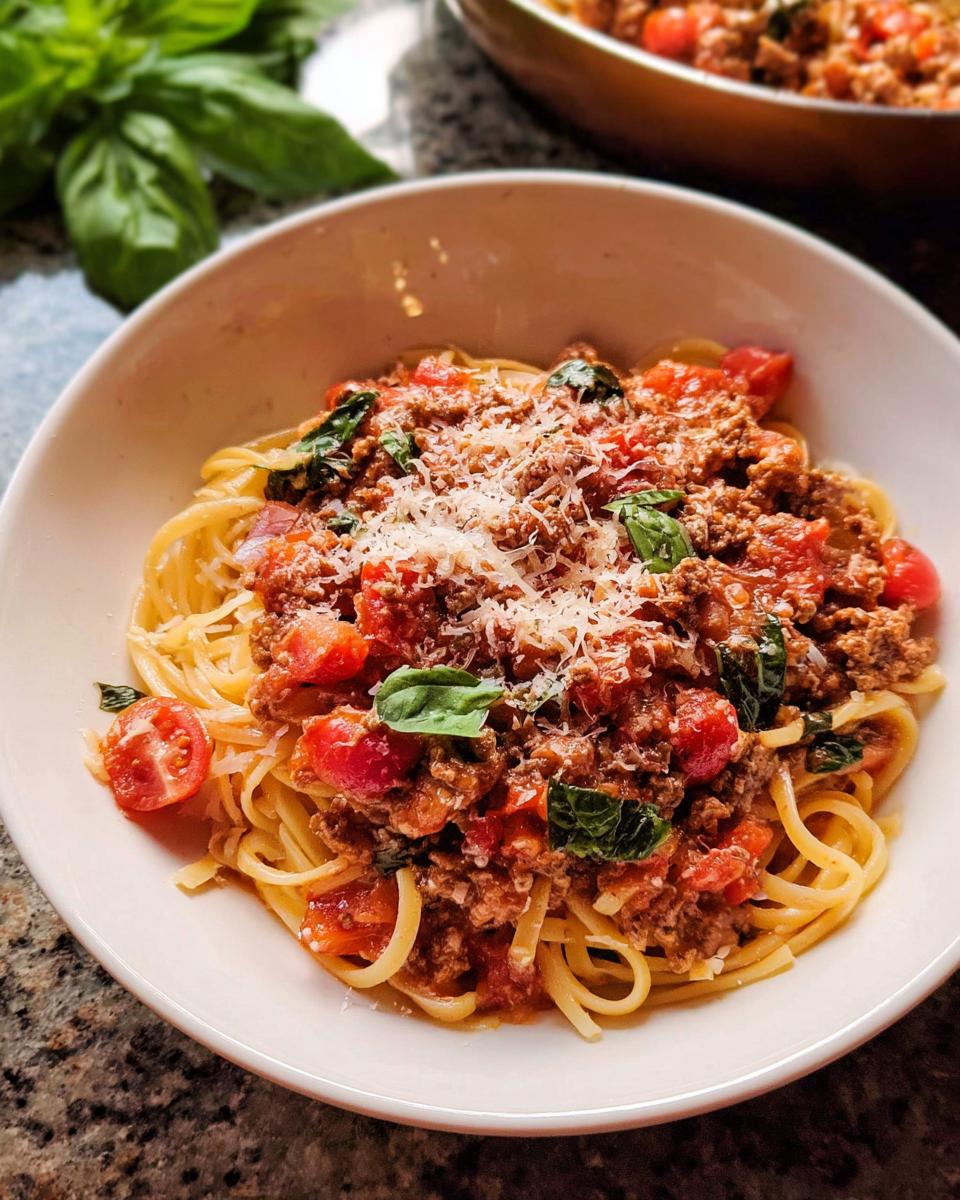 A bowl of spaghetti topped with hearty Turkey Bolognese sauce, fresh tomatoes, basil, and grated Parmesan cheese.