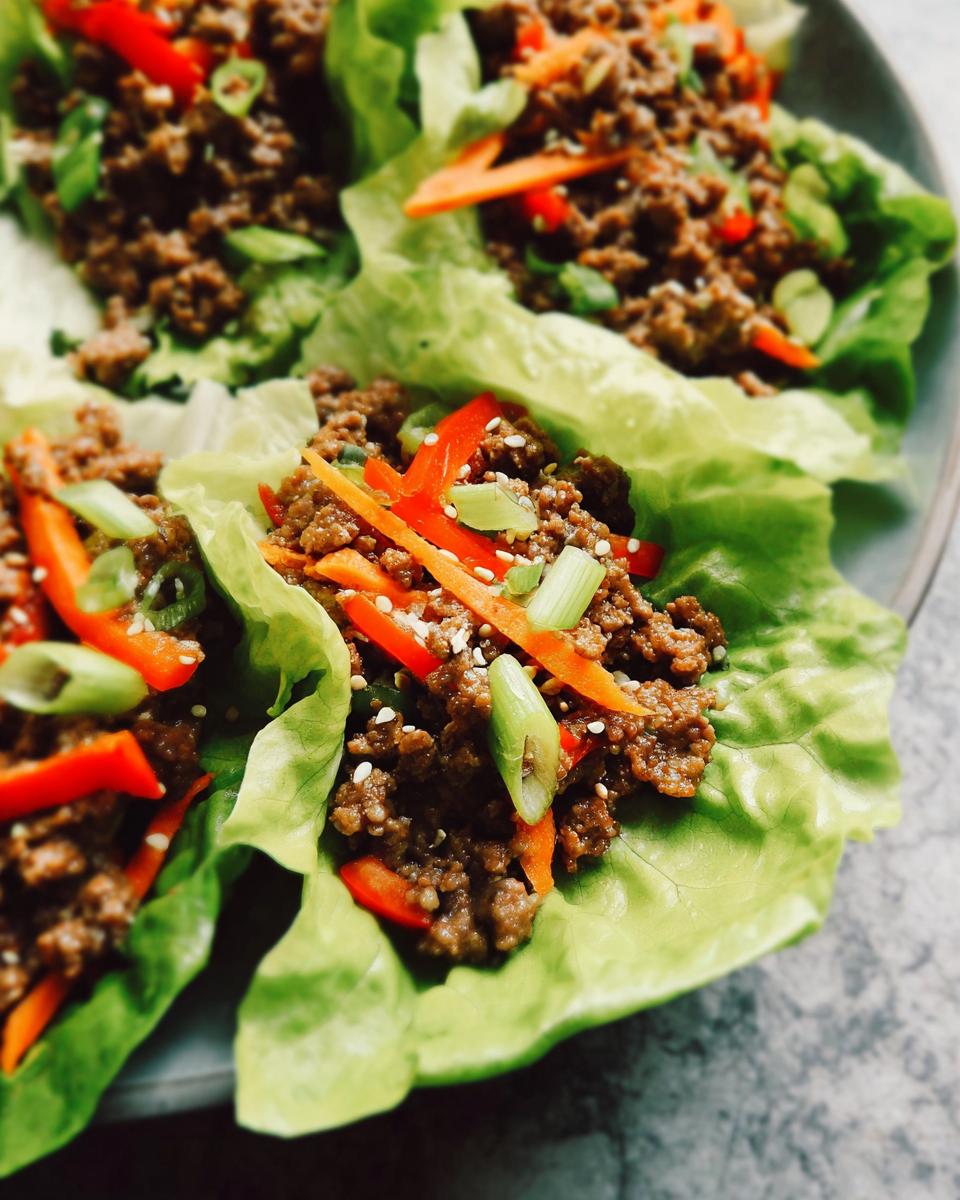 Close-up of three Asian Ground Beef Lettuce Wraps filled with seasoned ground beef, carrots, red peppers, and green onions.