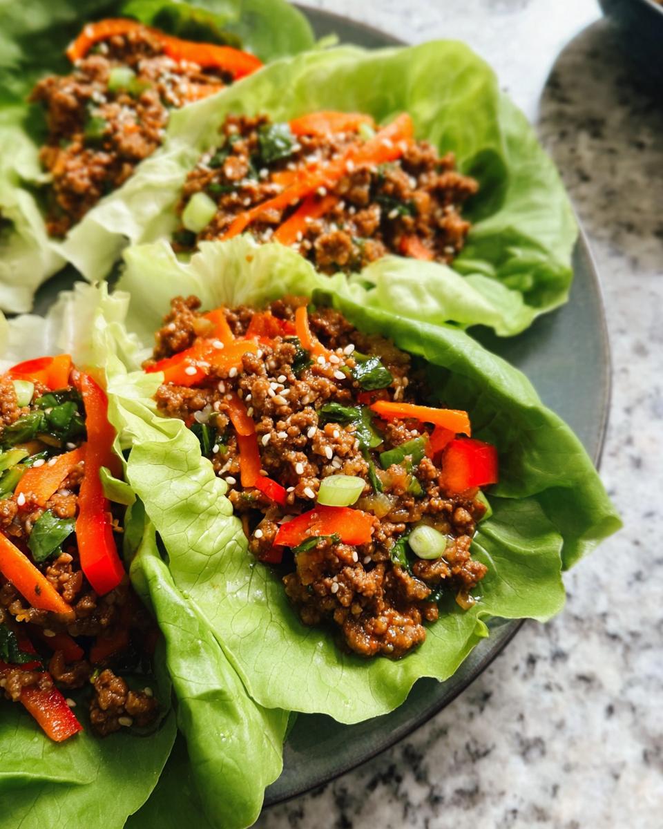 Close-up of three Asian Ground Beef Lettuce Wraps filled with savory ground meat, red peppers, and sesame seeds.