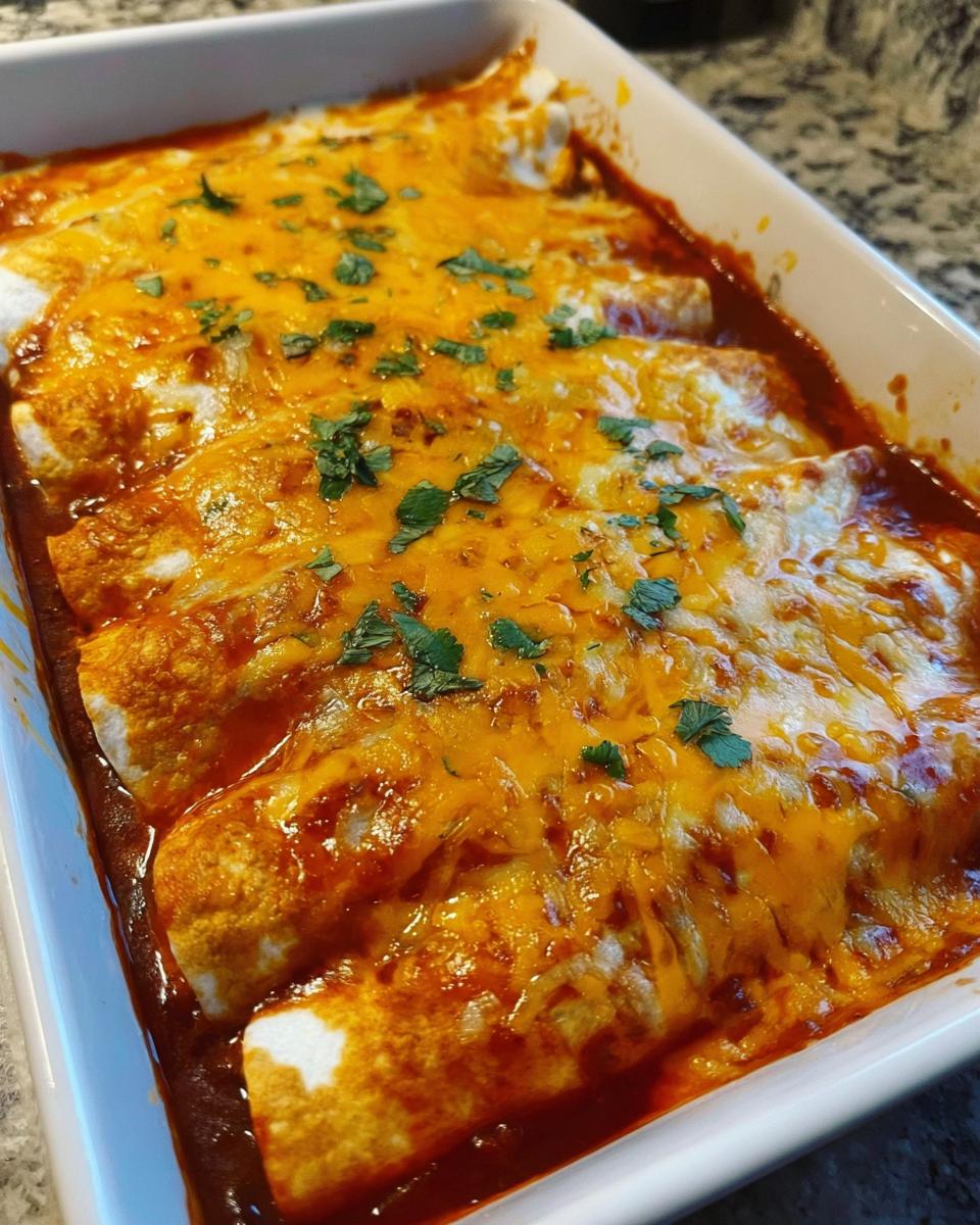 Close-up of freshly baked cheesy beef enchiladas covered in melted cheddar and sauce, garnished with cilantro.
