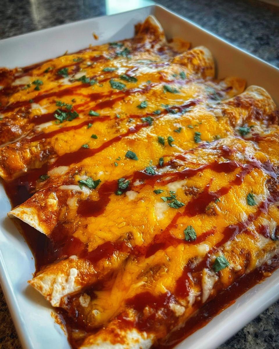 A close-up of baked cheesy beef enchiladas covered in melted cheddar cheese and red sauce, garnished with cilantro.