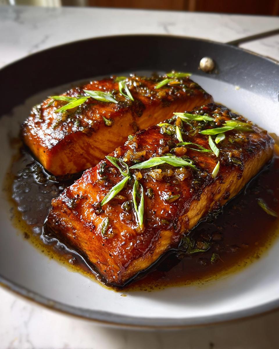 Two perfectly cooked Best Honey Garlic Baked Salmon Fillets glazed with a rich sauce and topped with fresh green onions.