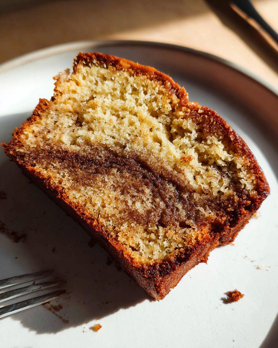Close-up of a moist slice of Cinnamon Swirl Banana Bread showing the rich cinnamon swirl center on a white plate.