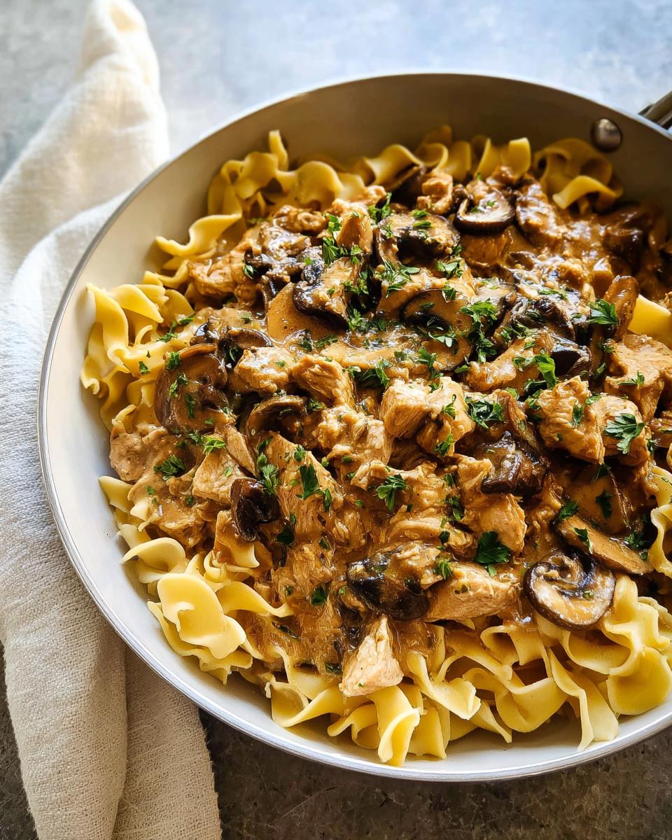 Close-up of Creamy Turkey Stroganoff with mushrooms served over wide egg noodles, garnished with parsley.