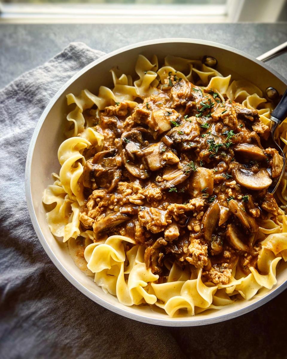 A skillet filled with Creamy Turkey Stroganoff sauce, mushrooms, and ground turkey served over wide egg noodles.