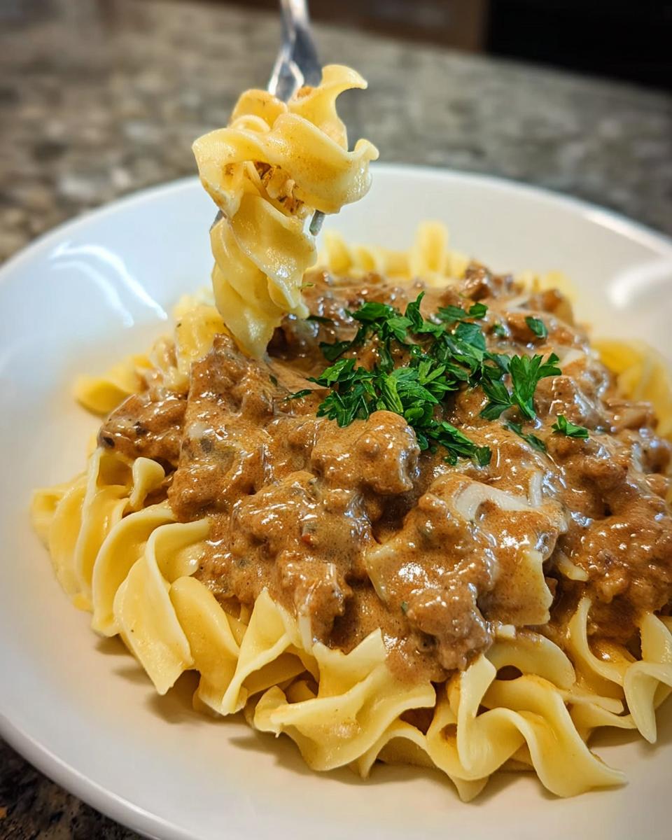 A fork lifts creamy turkey stroganoff and egg noodles from a white bowl, garnished with parsley.