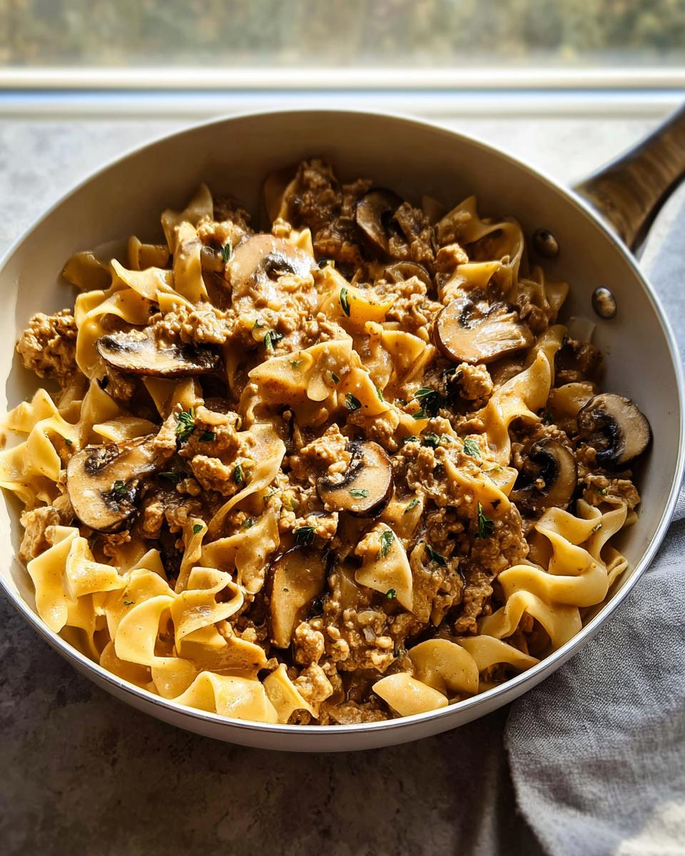 A skillet filled with Creamy Turkey Stroganoff mixed with wide egg noodles and sliced mushrooms, garnished with herbs