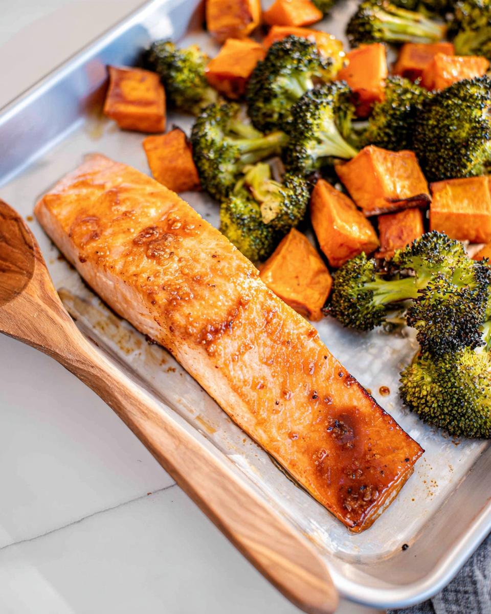 A close-up of a glazed Maple Dijon Salmon Sheet Pan Dinner with roasted broccoli and sweet potatoes.
