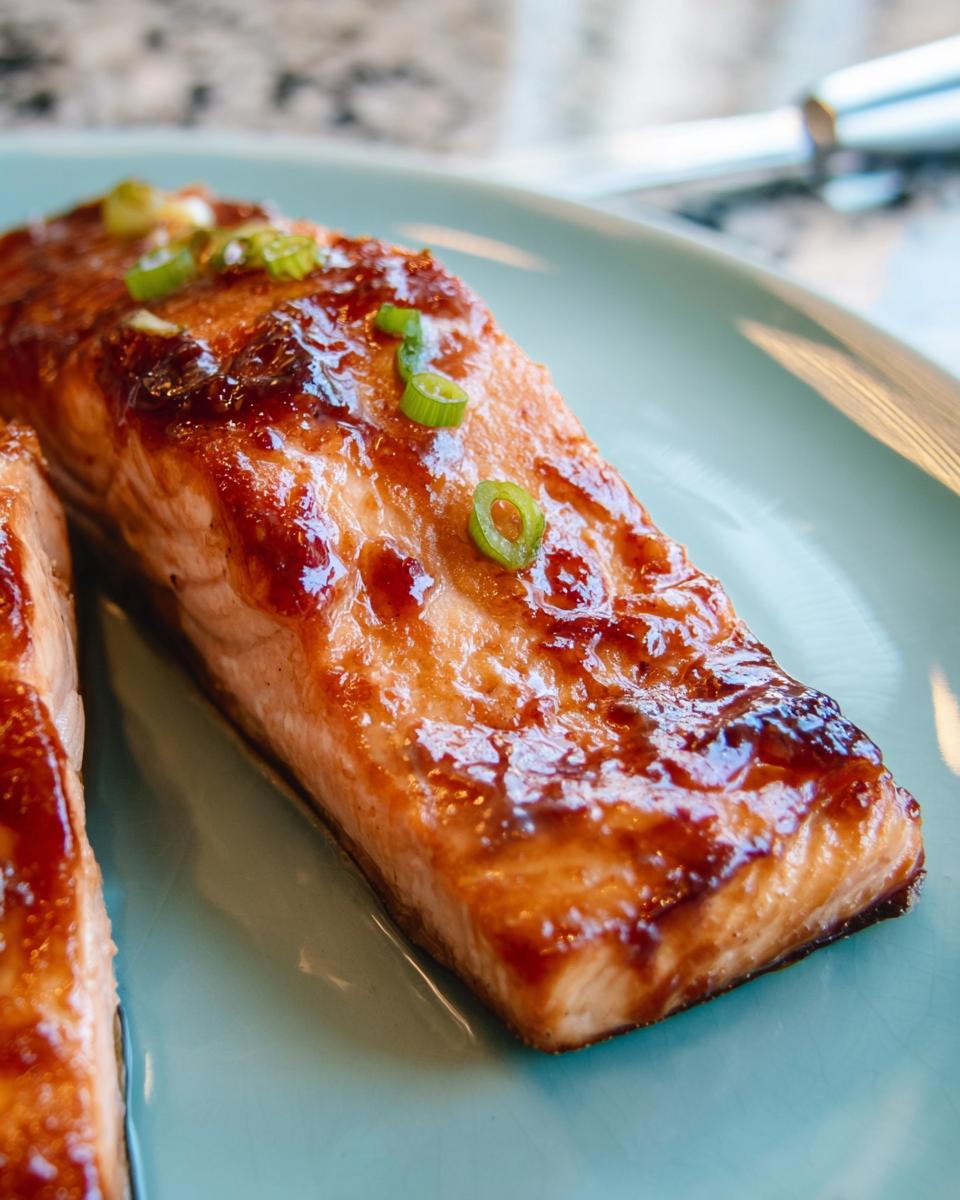 Close-up of a perfectly cooked Miso Glazed Broiled Salmon fillet topped with sliced green onions on a light blue plate.